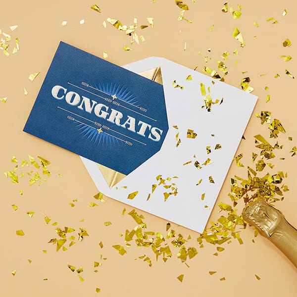 blue congratulations card falls out of white envelope with gold confetti all around it